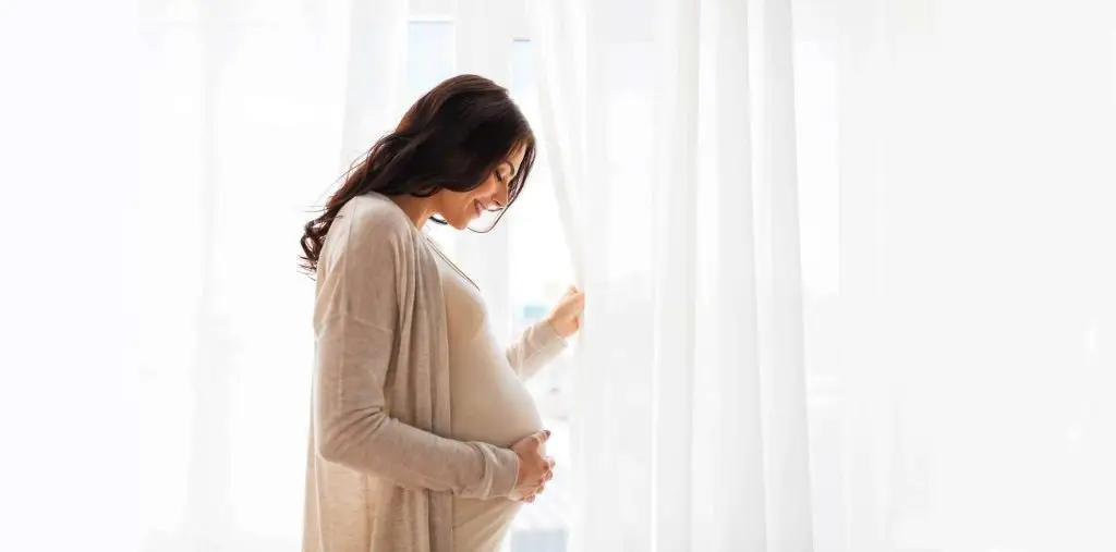 Photo of a pregnant woman smiling and holding her stomach